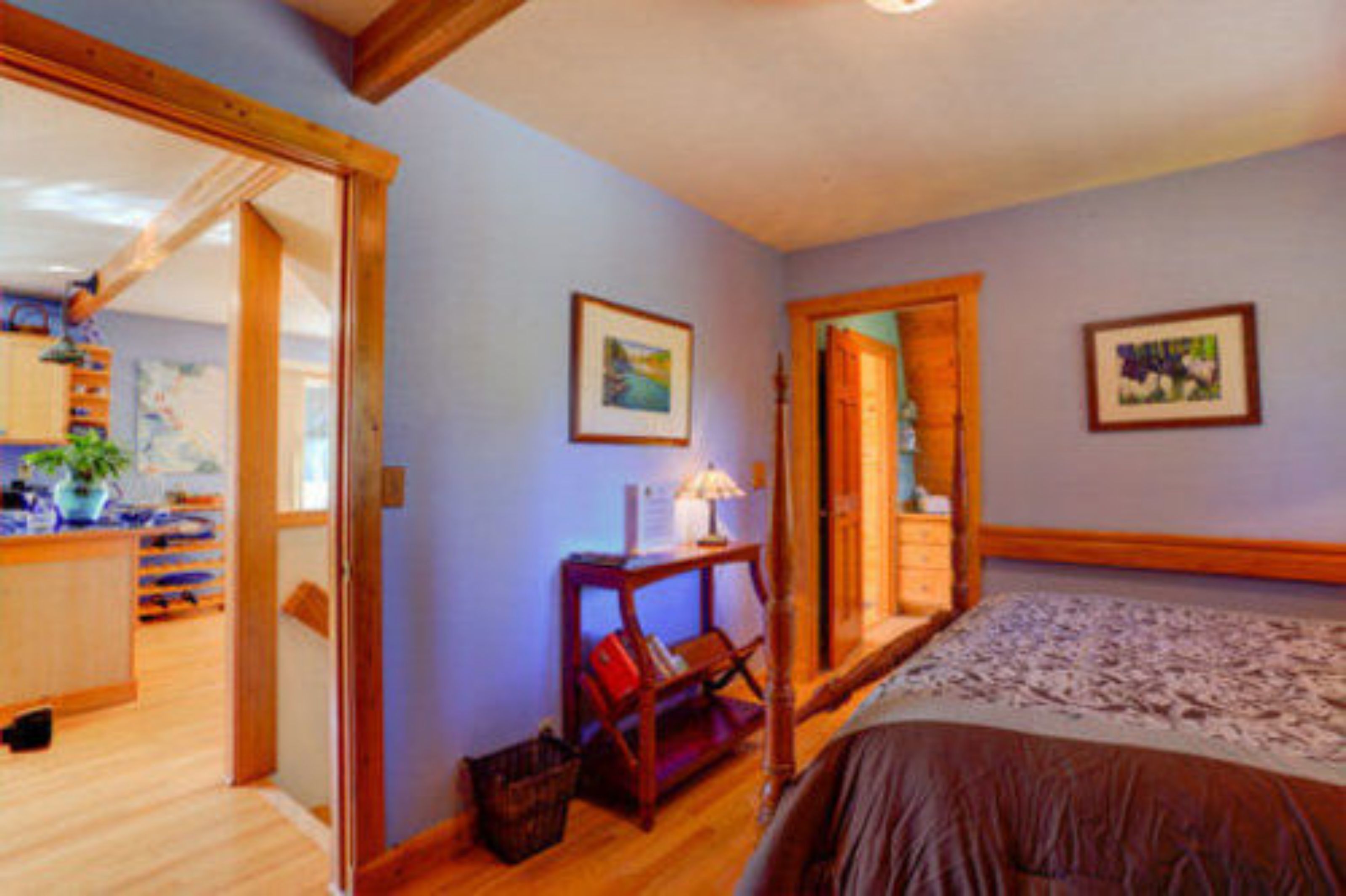 A bedroom with a bed, wooden floor, and a desk with a lamp.