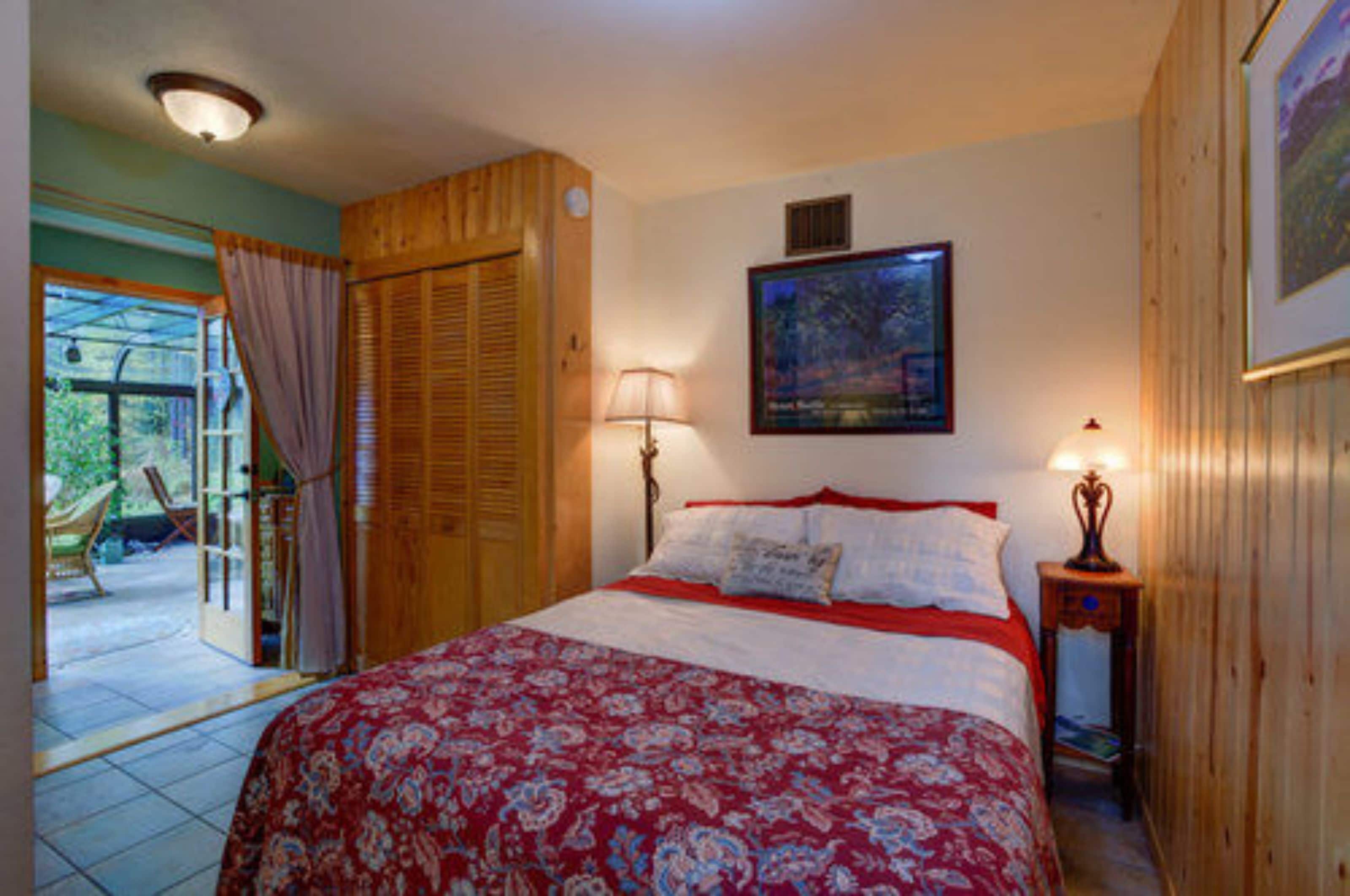 A bedroom with a bed, a nightstand, a lamp, a painting, and a wooden door.