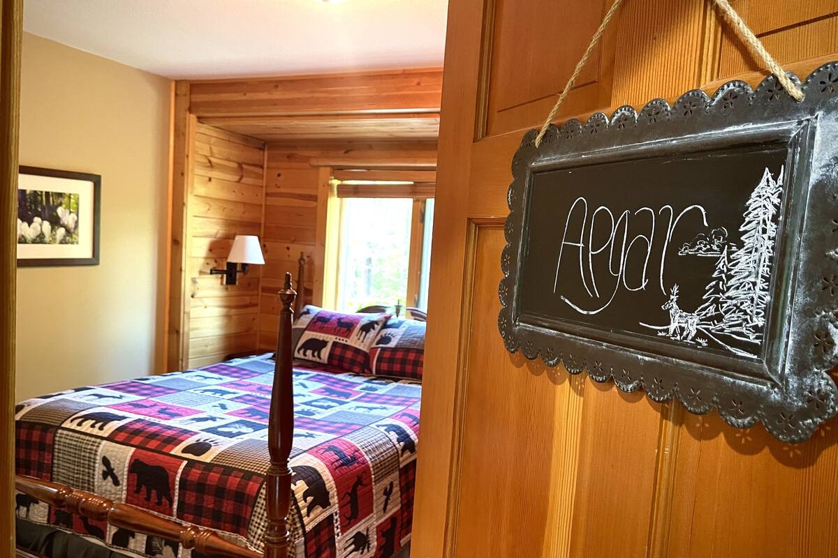 Una habitación acogedora con una cama que tiene un colcha de colores, un cabecero de madera y un cartel en la pared con una ilustración de un ciervo y árboles.