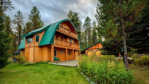 Une cabane en bois avec un toit vert, un balcon et une véranda.