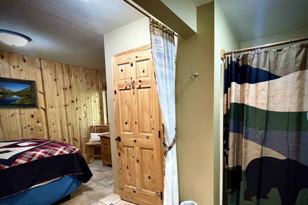 Una habitación con cama, armario de madera, cortina, alfombra y un cuadro en la pared.