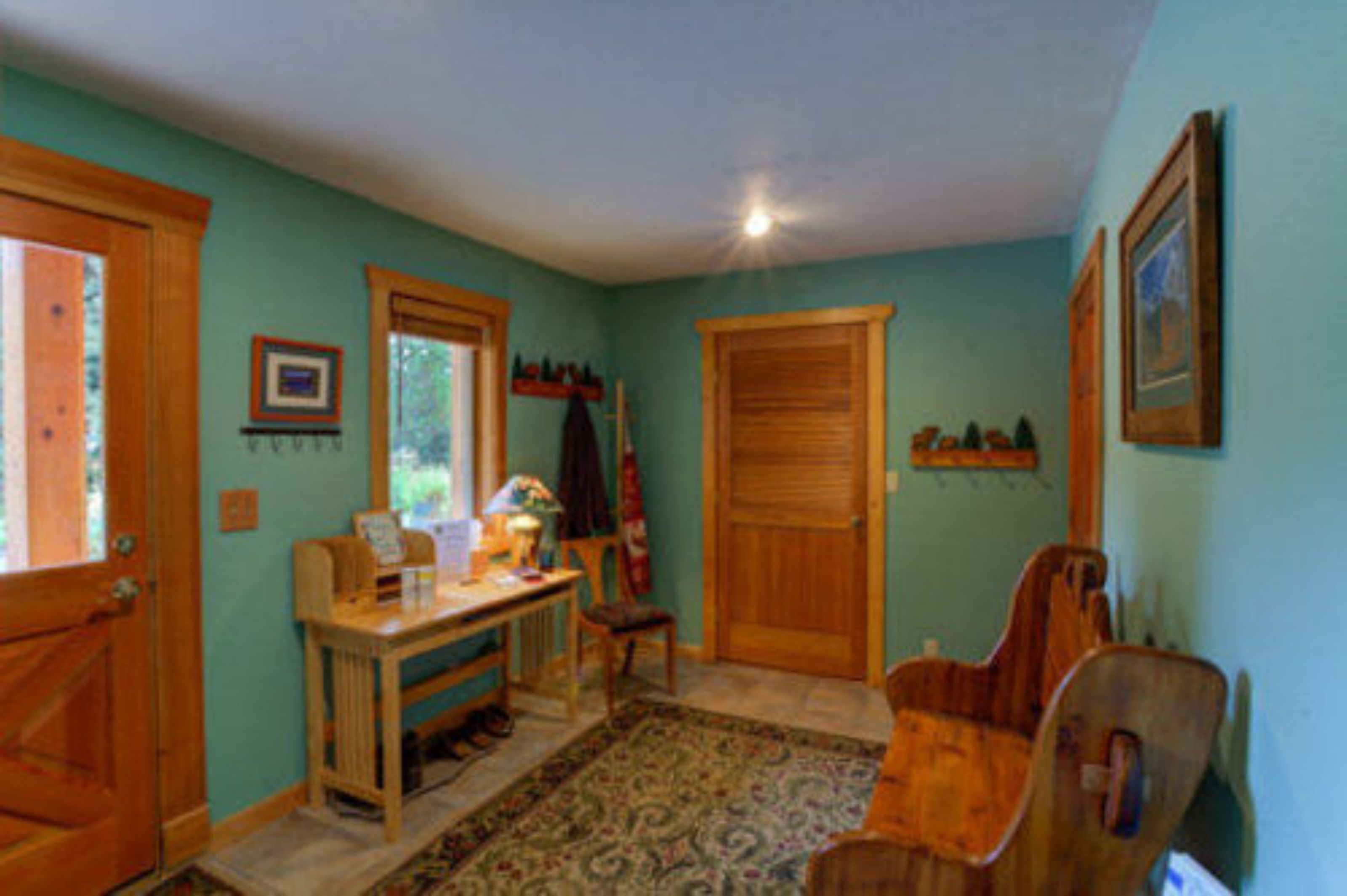A room with a wooden desk, chair, and a rug. There are two doors and a window.
