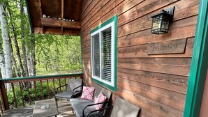 A wooden deck with two gray chairs and a small table, a window with a green frame, and a nameplate reading "Hunter". - Chinook Wind Cabins (Talkeetna)