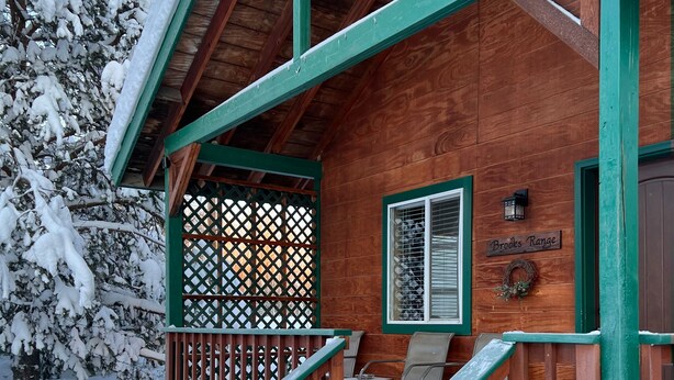 A wooden cabin with a covered porch, a sign reading "Brooks Range," and a staircase leading to the entrance. - Chinook Wind Cabins (Talkeetna)