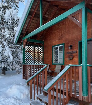 A wooden cabin with a covered porch, a sign reading "Brooks Range," and a staircase leading to the entrance. - Chinook Wind Cabins (Talkeetna)