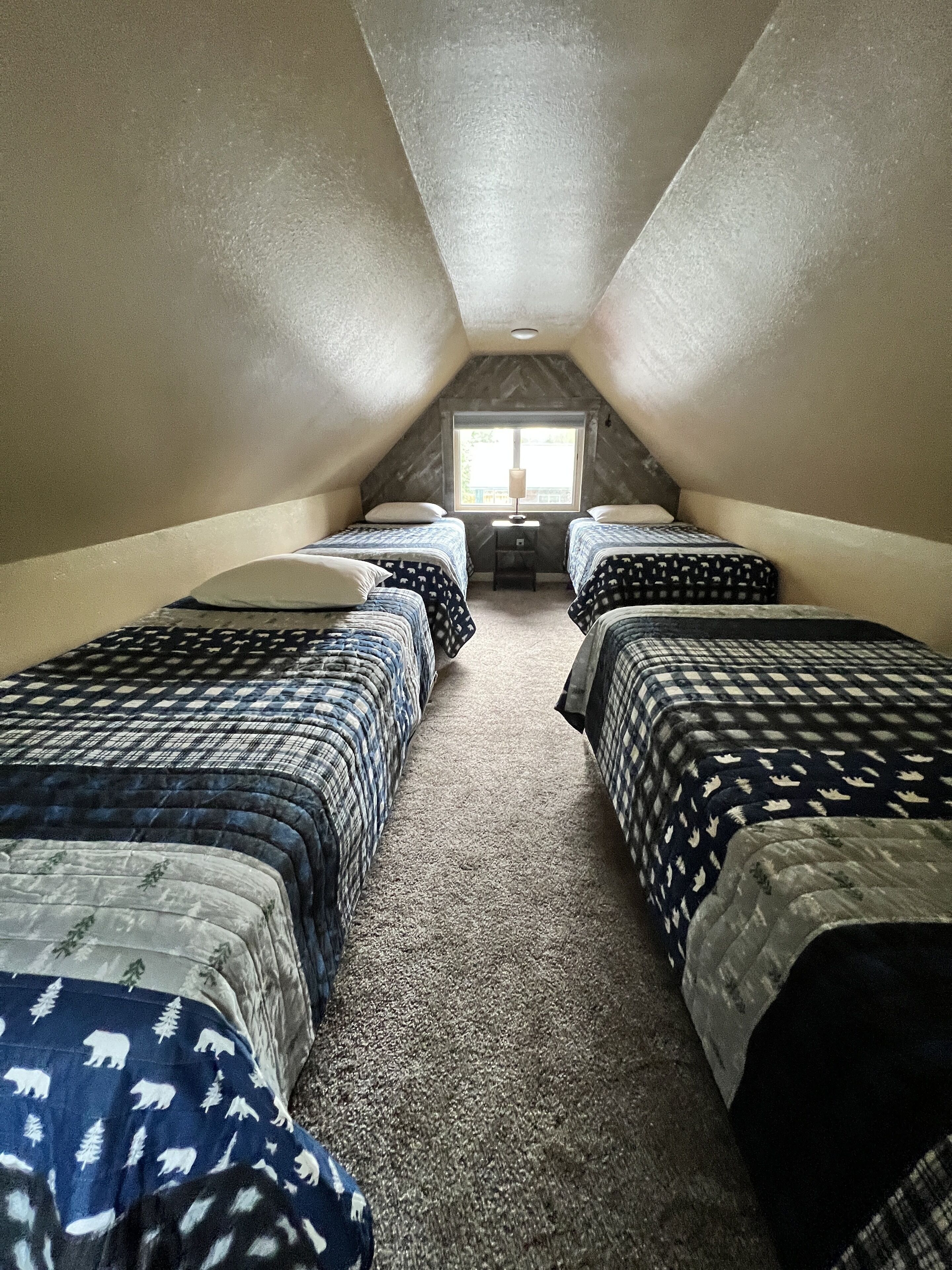 A small, triangular attic bedroom with two beds, a window, and a nightstand.