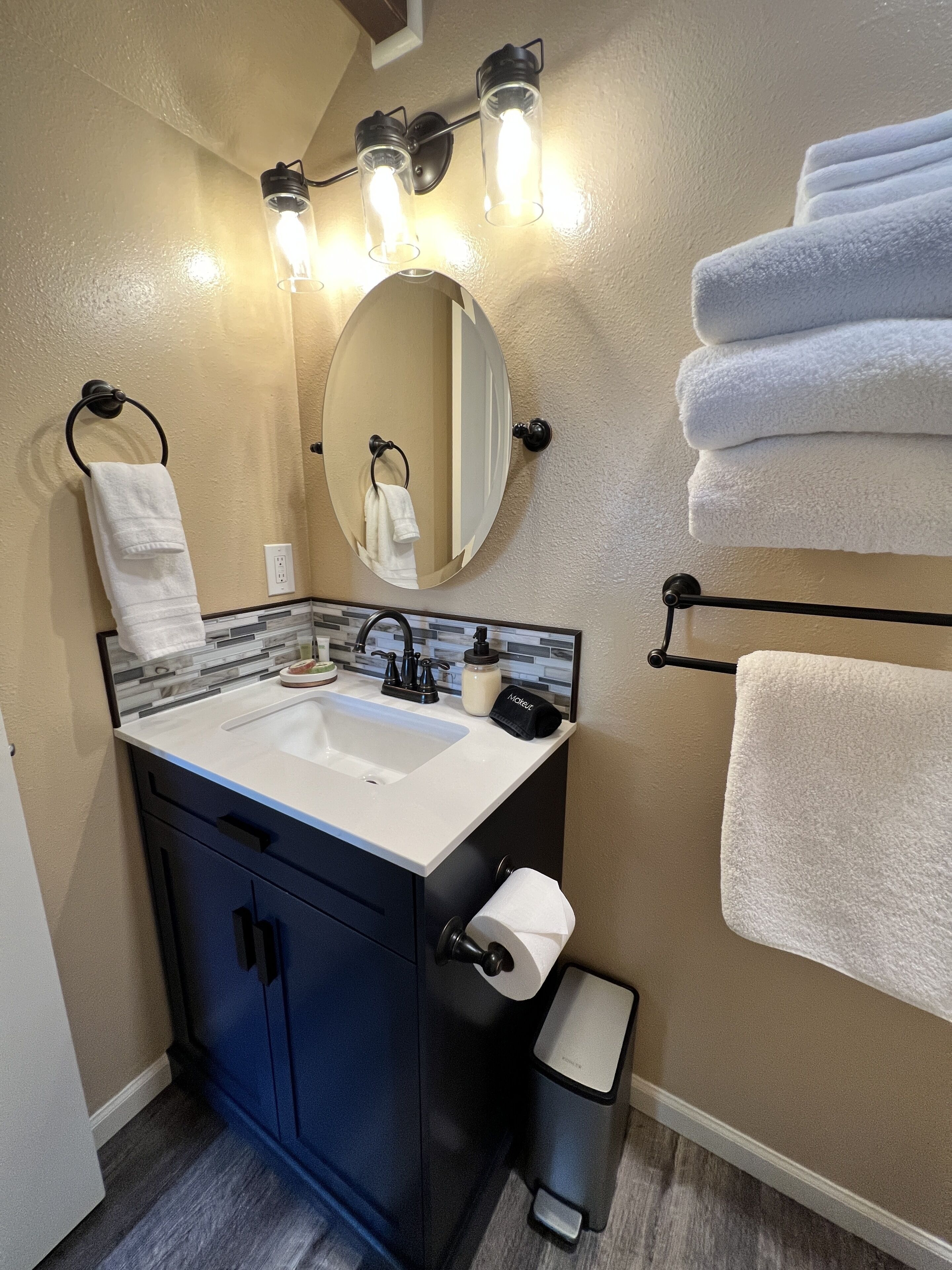 A modern bathroom with a sink, mirror, towel rack, and a trash bin.
