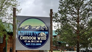 A sign for Chinook Wind Cabins with a mountain and cabin illustration. - Chinook Wind Cabins (Talkeetna)