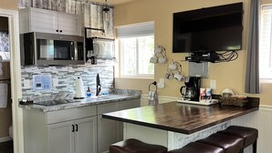 A compact kitchen with a built-in microwave, a coffee maker, and a flat-screen TV mounted above the counter. - Chinook Wind Cabins (Talkeetna)