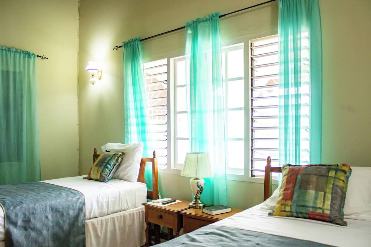Une chambre d’hôtel avec deux lits, une table de chevet, une lampe et une fenêtre avec des rideaux.