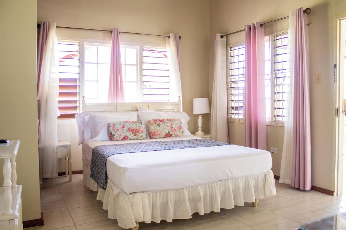 Une chambre à coucher avec un lit, des rideaux, une table de chevet et une fenêtre avec des stores.