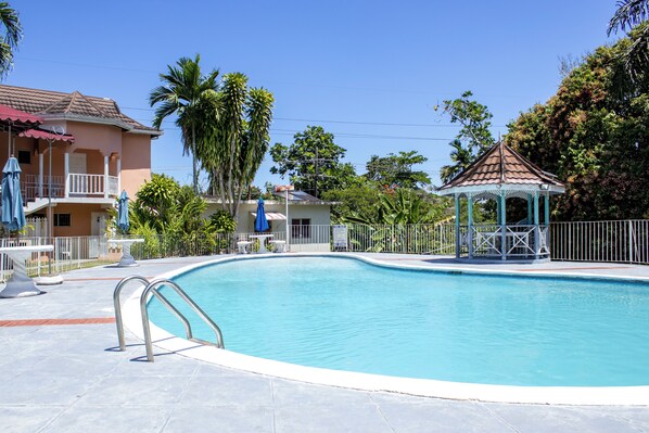 A swimming pool with a gazebo, palm trees, and a building with a balcony.