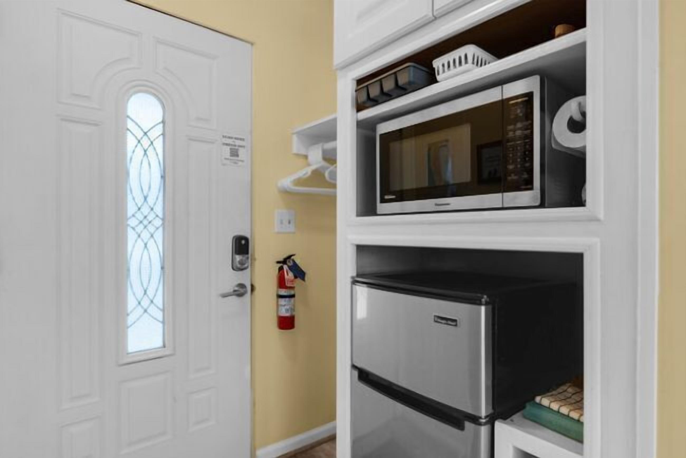 A compact kitchen with a microwave, refrigerator, and a fire extinguisher mounted on the wall.