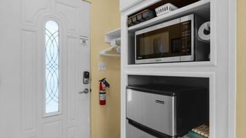 A compact kitchen with a microwave, refrigerator, and a fire extinguisher mounted on the wall.