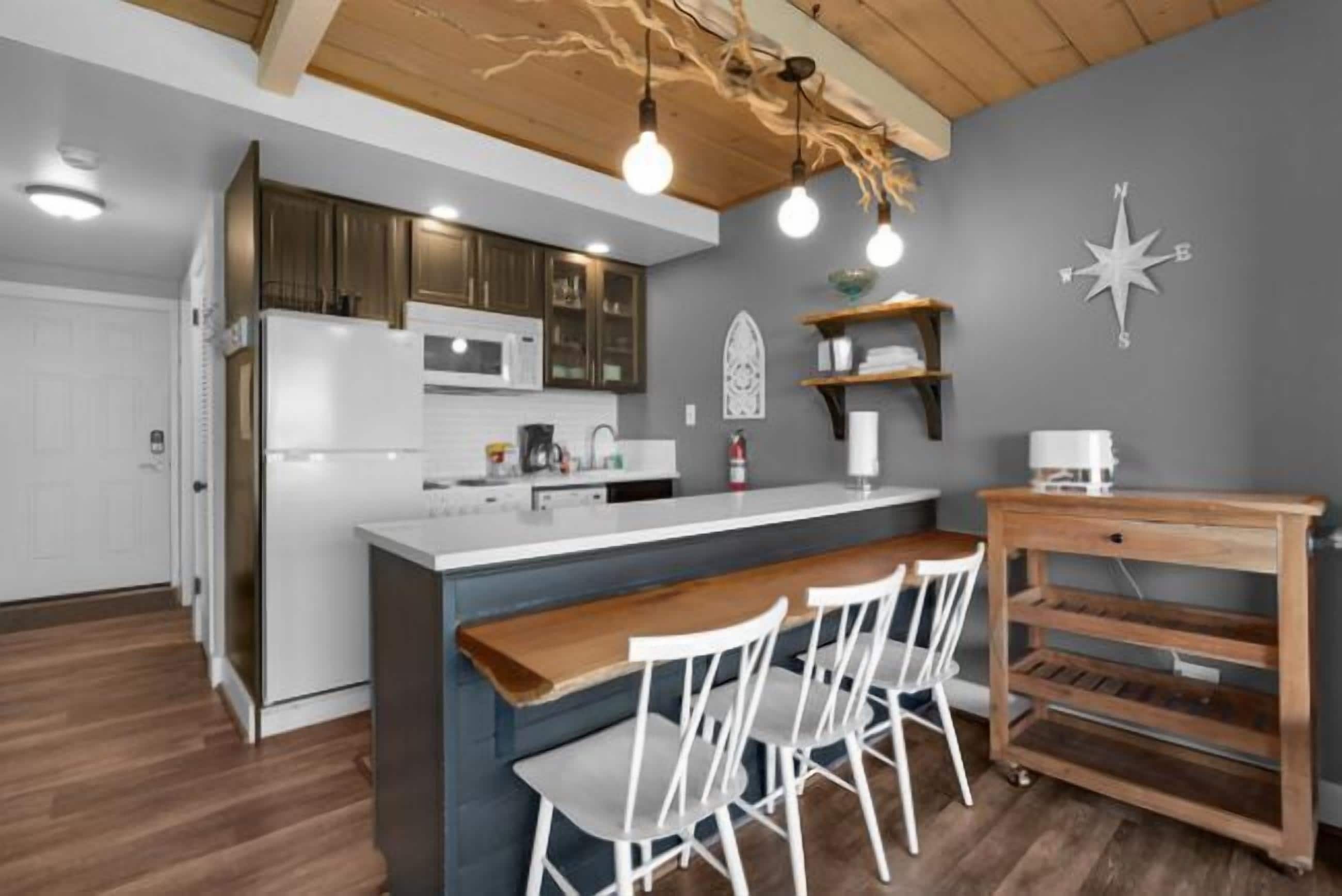 Een moderne keuken met een centraal eiland, witte stoelen, houten planken en een decoratieve kompaswand.