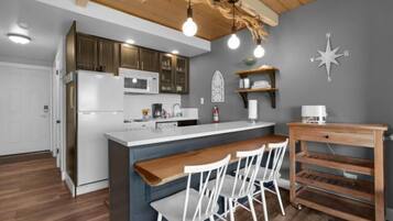 Een moderne keuken met een centraal eiland, witte stoelen, houten planken en een decoratieve kompaswand.