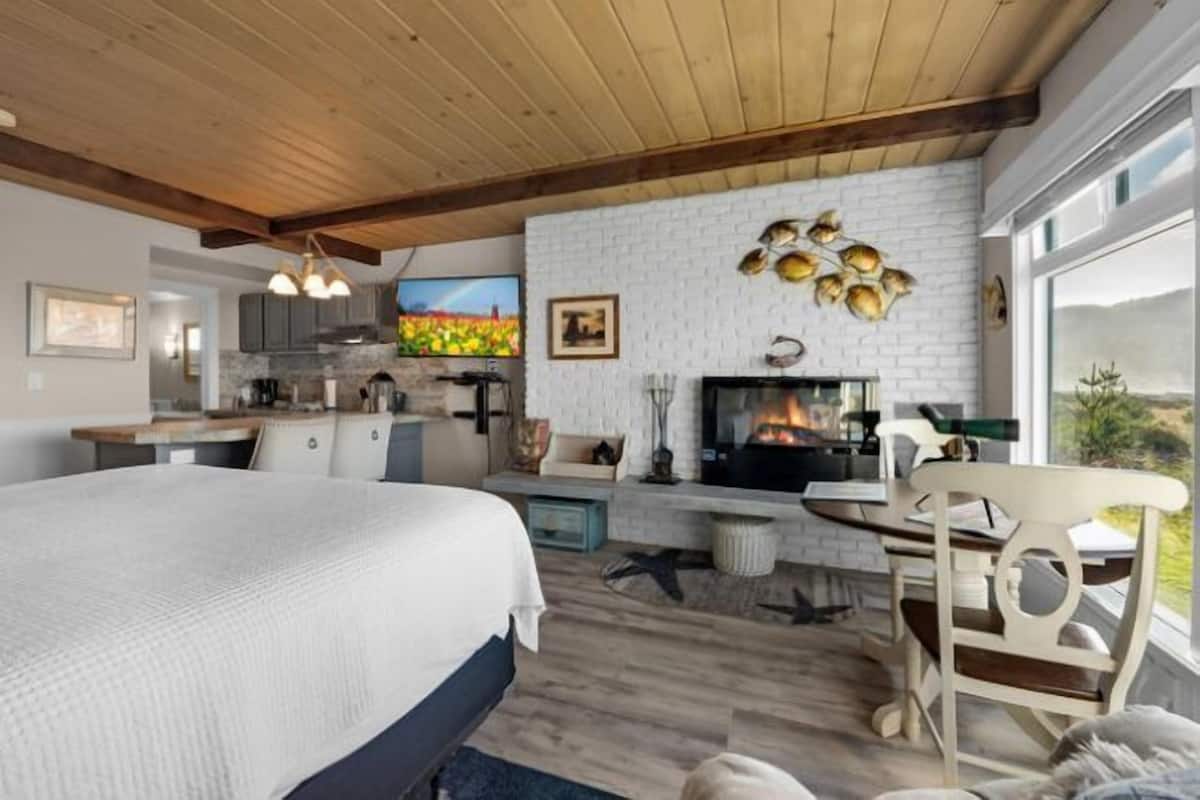 A modern bedroom with a large bed, a fireplace, and a view of the outdoors.