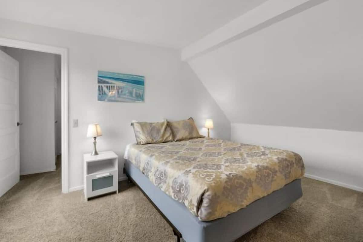 A bedroom with a bed, a nightstand, a lamp, and a painting on the wall.