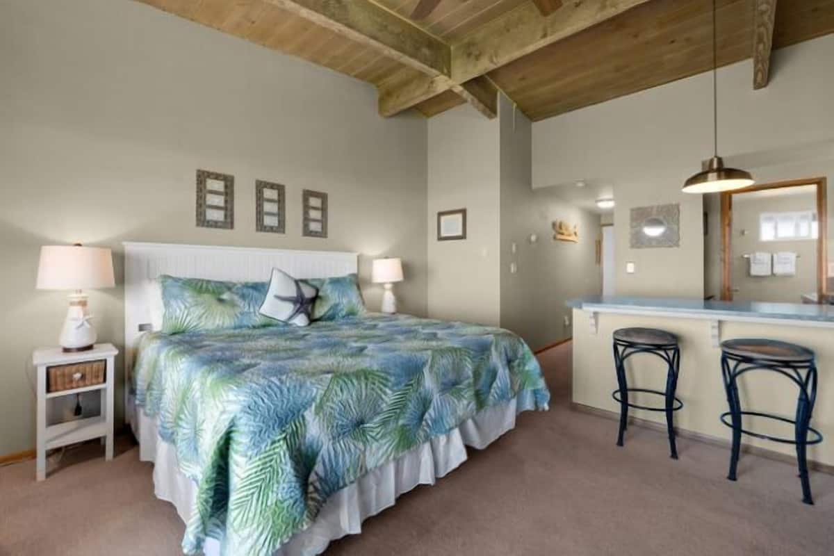 A bedroom with a bed, nightstands, a desk with two stools, and a mirror.
