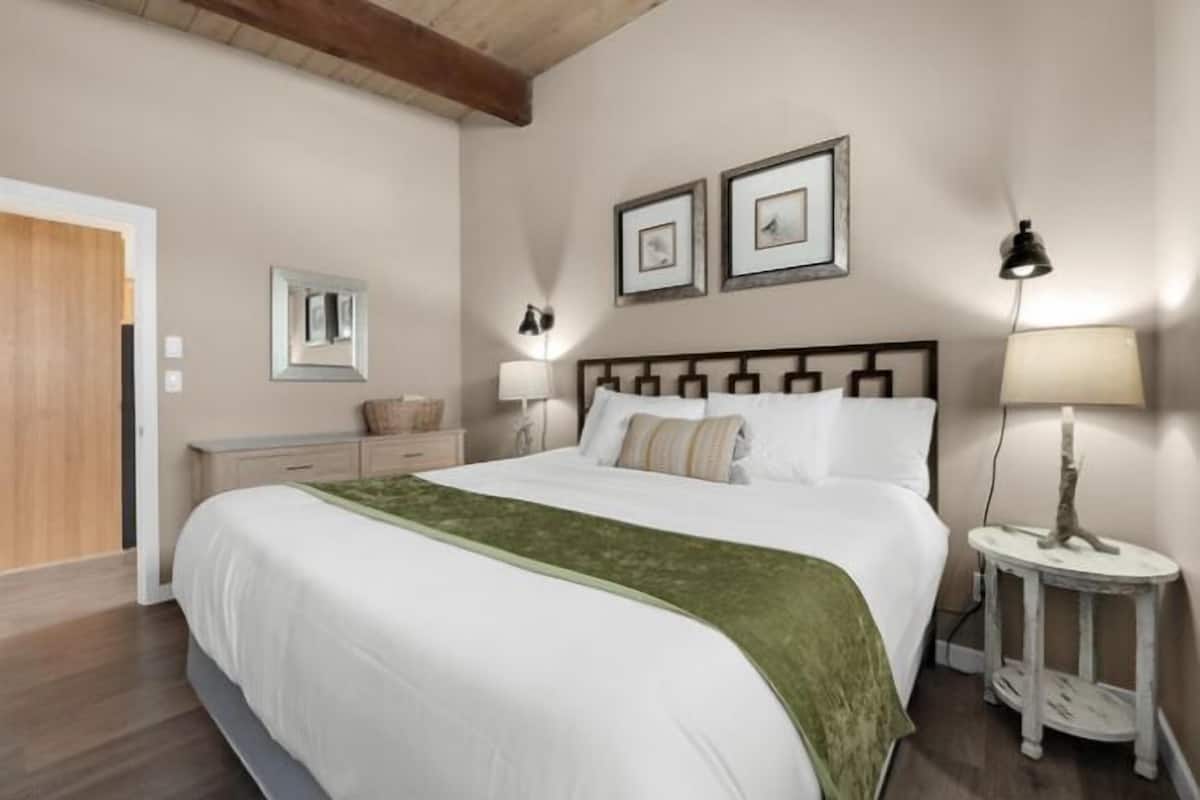 A bedroom with a large bed, a bedside table with a lamp, a dresser, and two framed pictures on the wall.