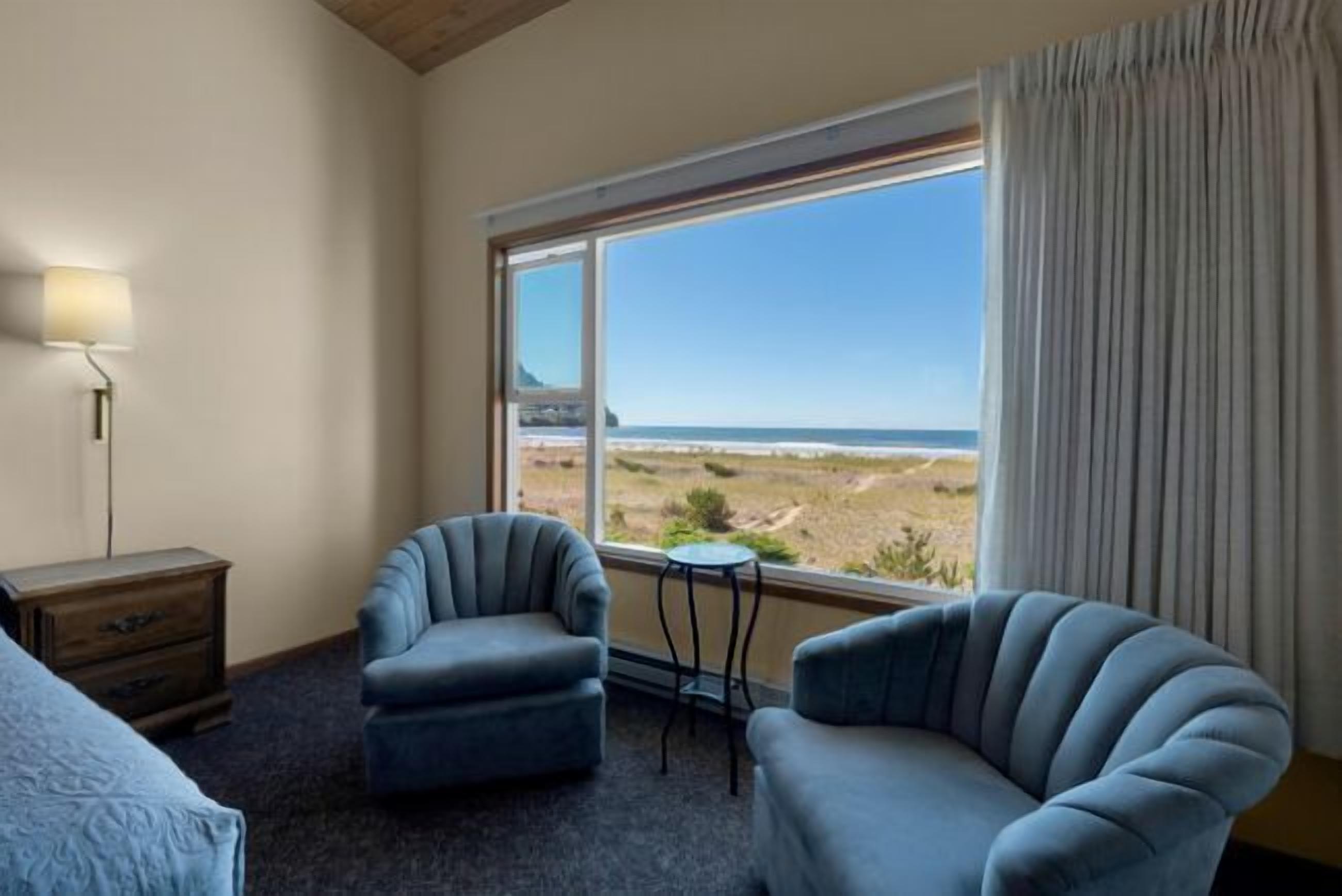 Ein Zimmer mit zwei Sesseln, einem kleinen Tisch, einer Lampe und Blick auf den Strand.