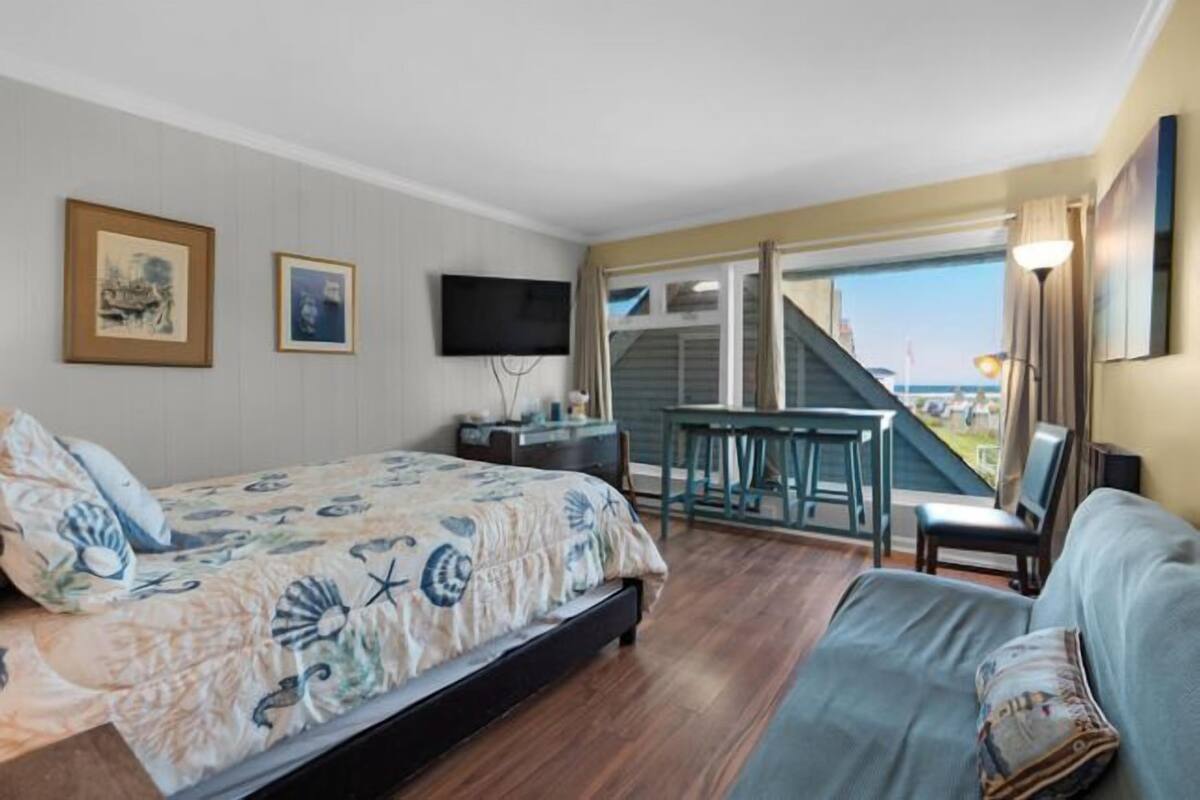 A bedroom with a bed, a desk, a chair, and a balcony with a view.