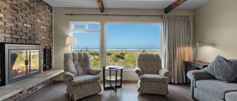 A living room with a fireplace, two armchairs, a sofa, a coffee table, and a view of the outdoors.