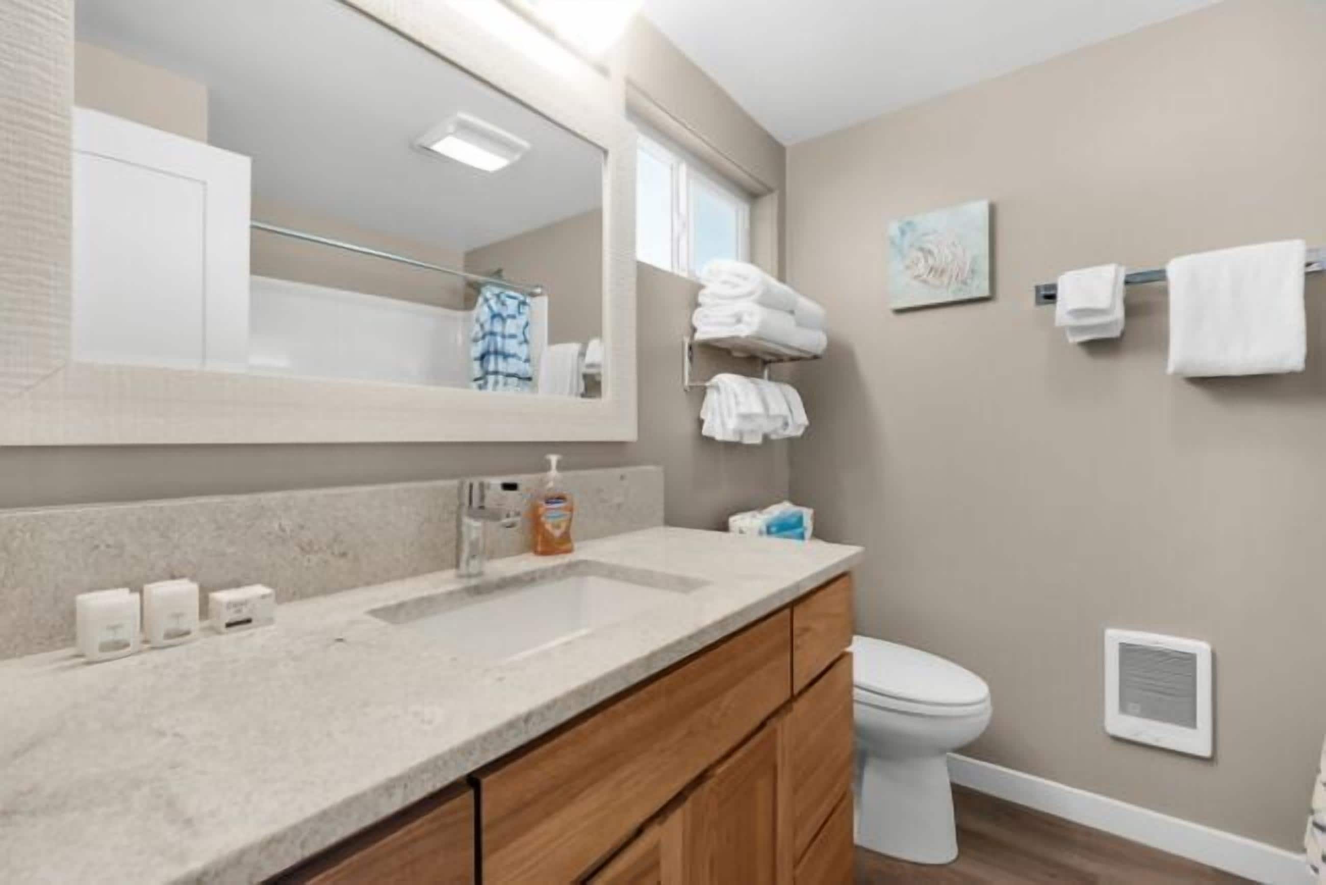 A modern bathroom with a large mirror, a sink with soap dispensers, a toilet, and neatly folded towels on a rack.