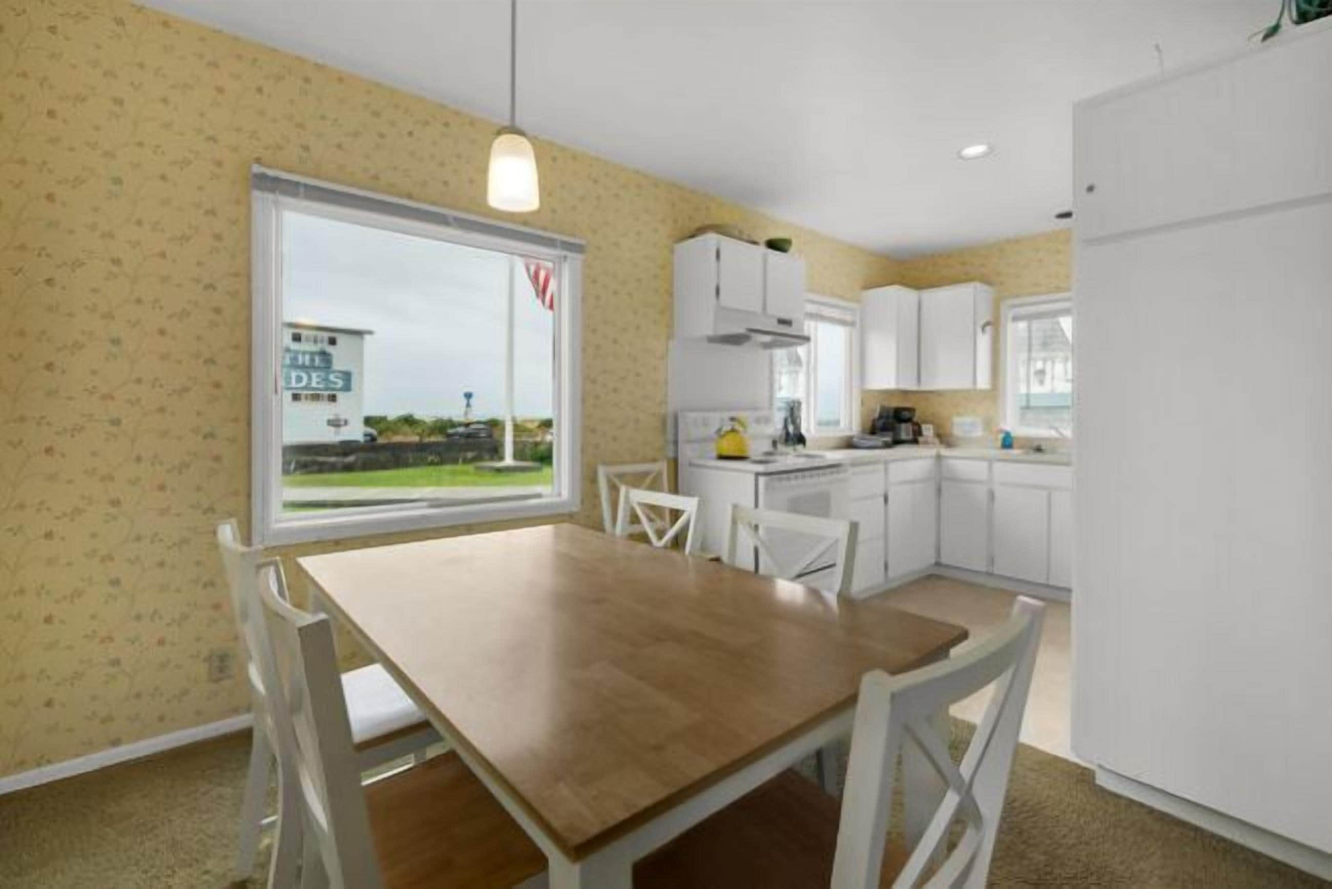Una cocina compacta con armarios blancos, una mesa de comedor con sillas y un ventanal con vista a un edificio.
