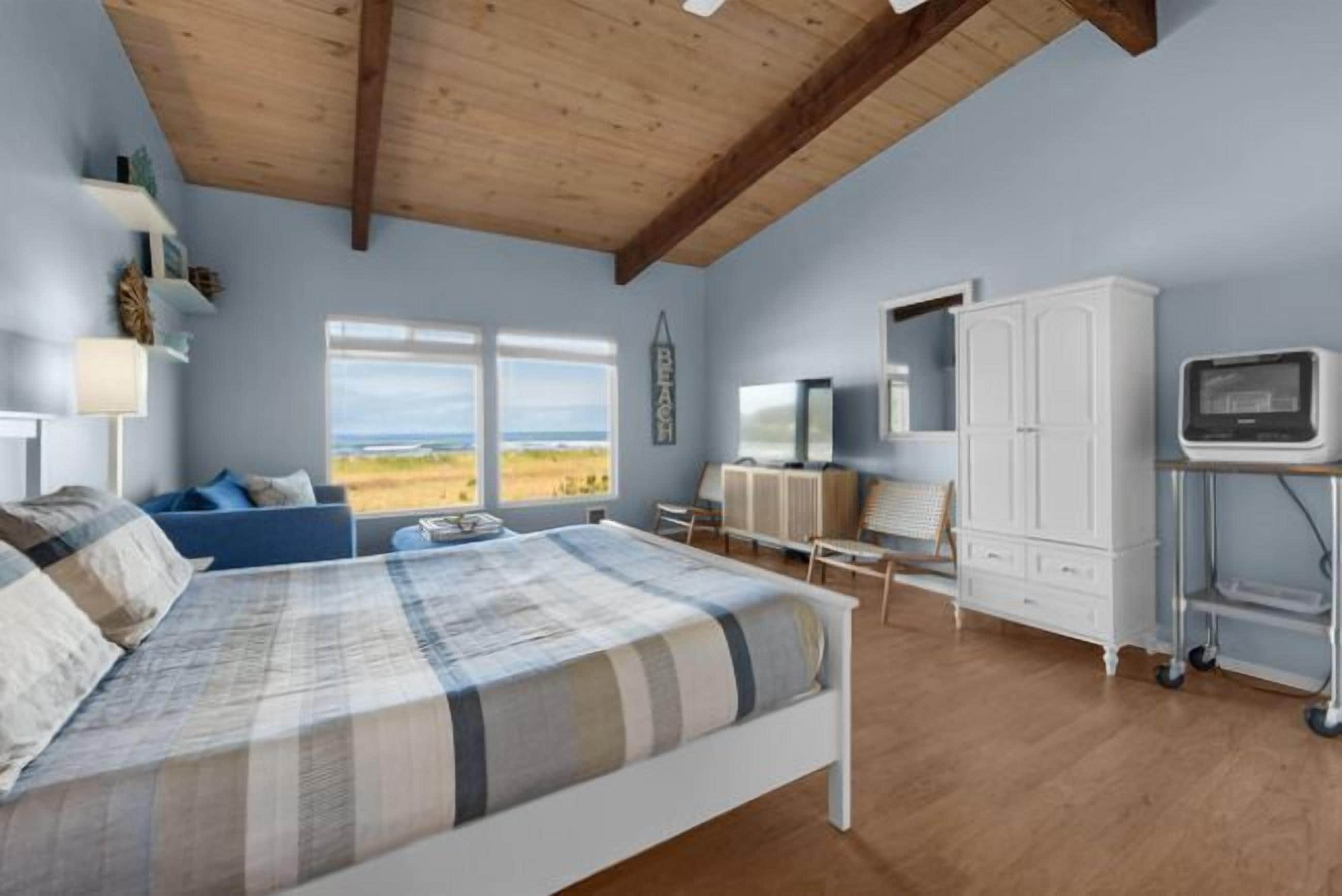 Ein Schlafzimmer mit Bett, Schreibtisch, Fernseher und Blick ins Freie.