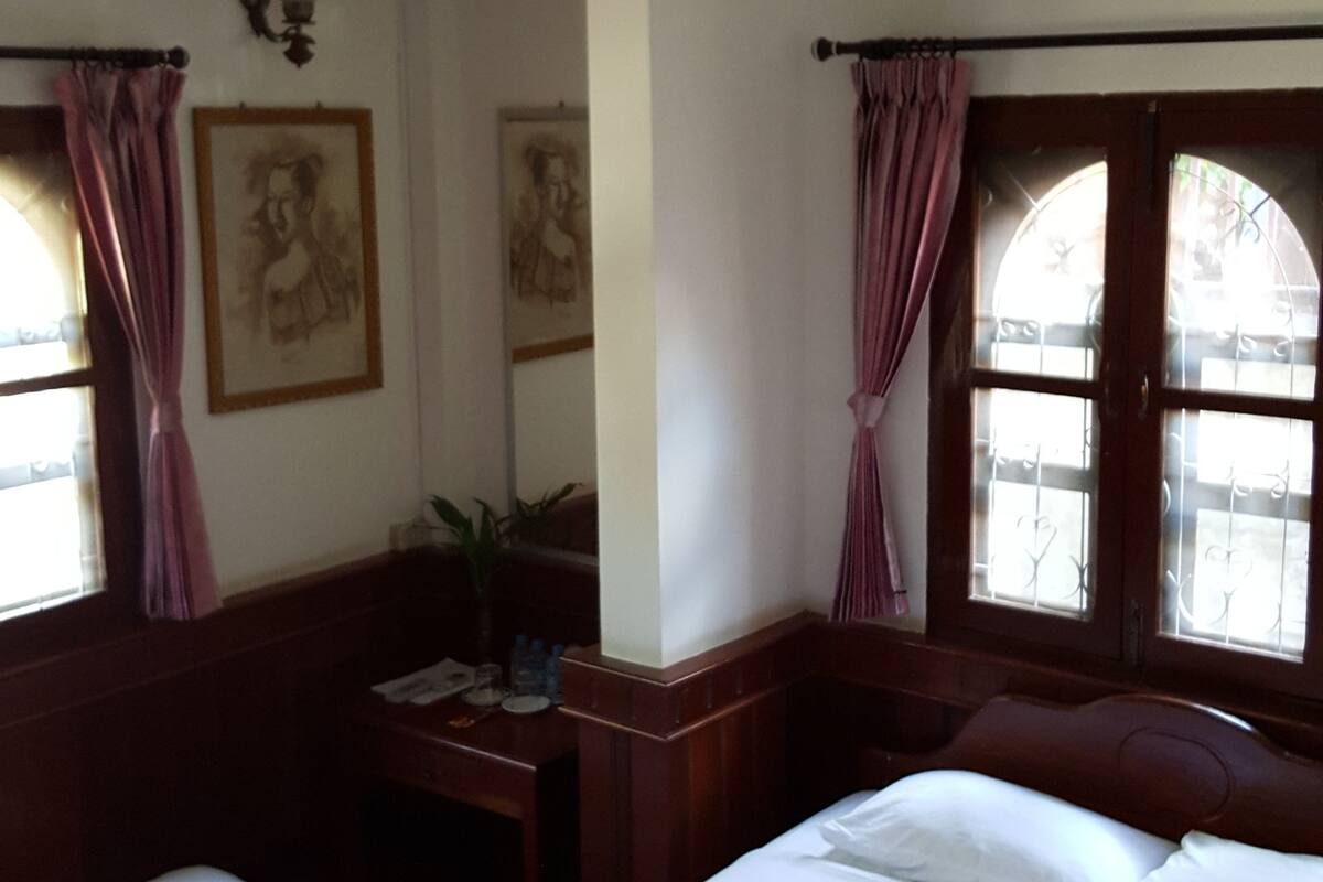A hotel room with two beds, a ceiling fan, a wall-mounted air conditioner, and a window with curtains.