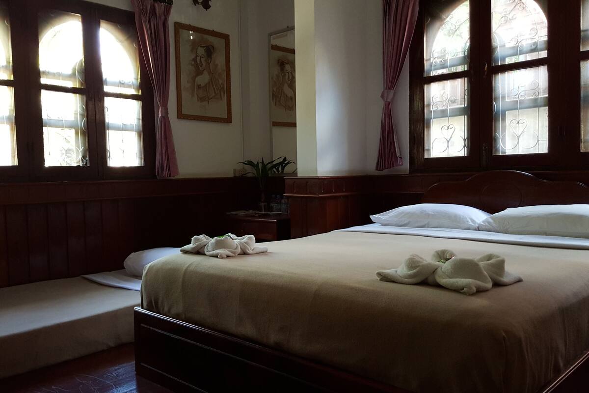A hotel room with a large bed, a bedside table, and a window with curtains.