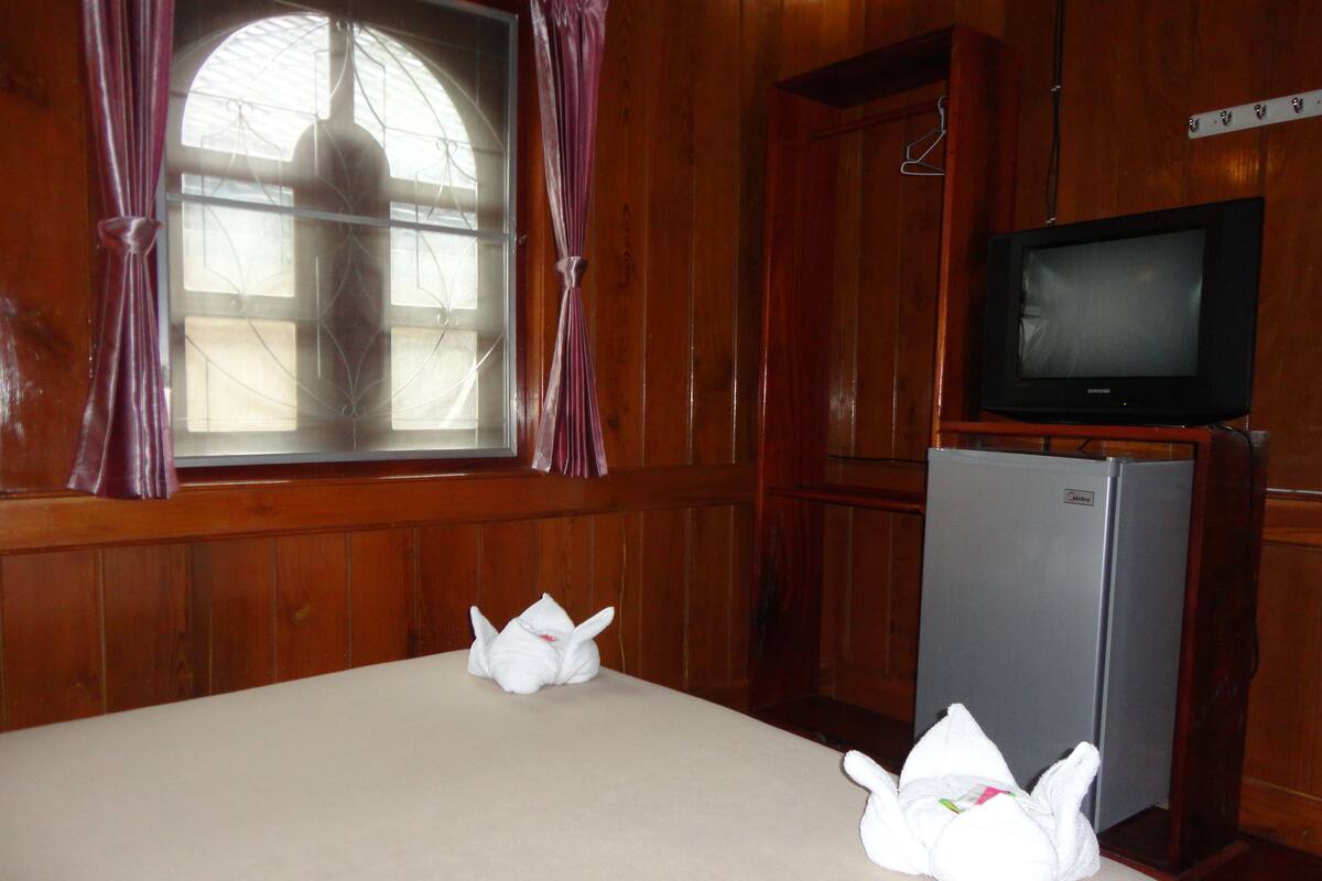 A room with a bed, a television on a stand, and a window with curtains.