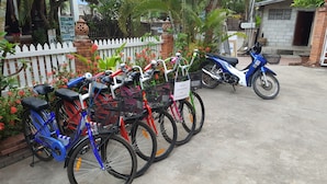 A row of bicycles parked in front of a building with a white picket fence, a brick wall, and some greenery. - Villa Philaylack (Luang Prabang)