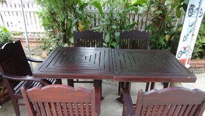 A patio area with a wooden table and chairs, surrounded by a white picket fence and lush greenery. - Villa Philaylack (Luang Prabang)