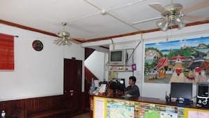 A reception area with a wooden counter, a television, a ceiling fan, and a mural on the wall. - Villa Philaylack (Luang Prabang)