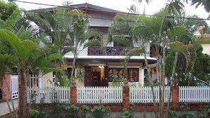 A two-story house with a white picket fence, surrounded by lush greenery and palm trees. - Villa Philaylack (Luang Prabang)