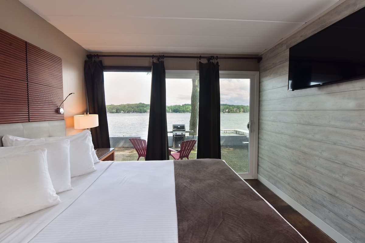 A hotel room with a bed, a TV, a window with curtains, and a view of a body of water.