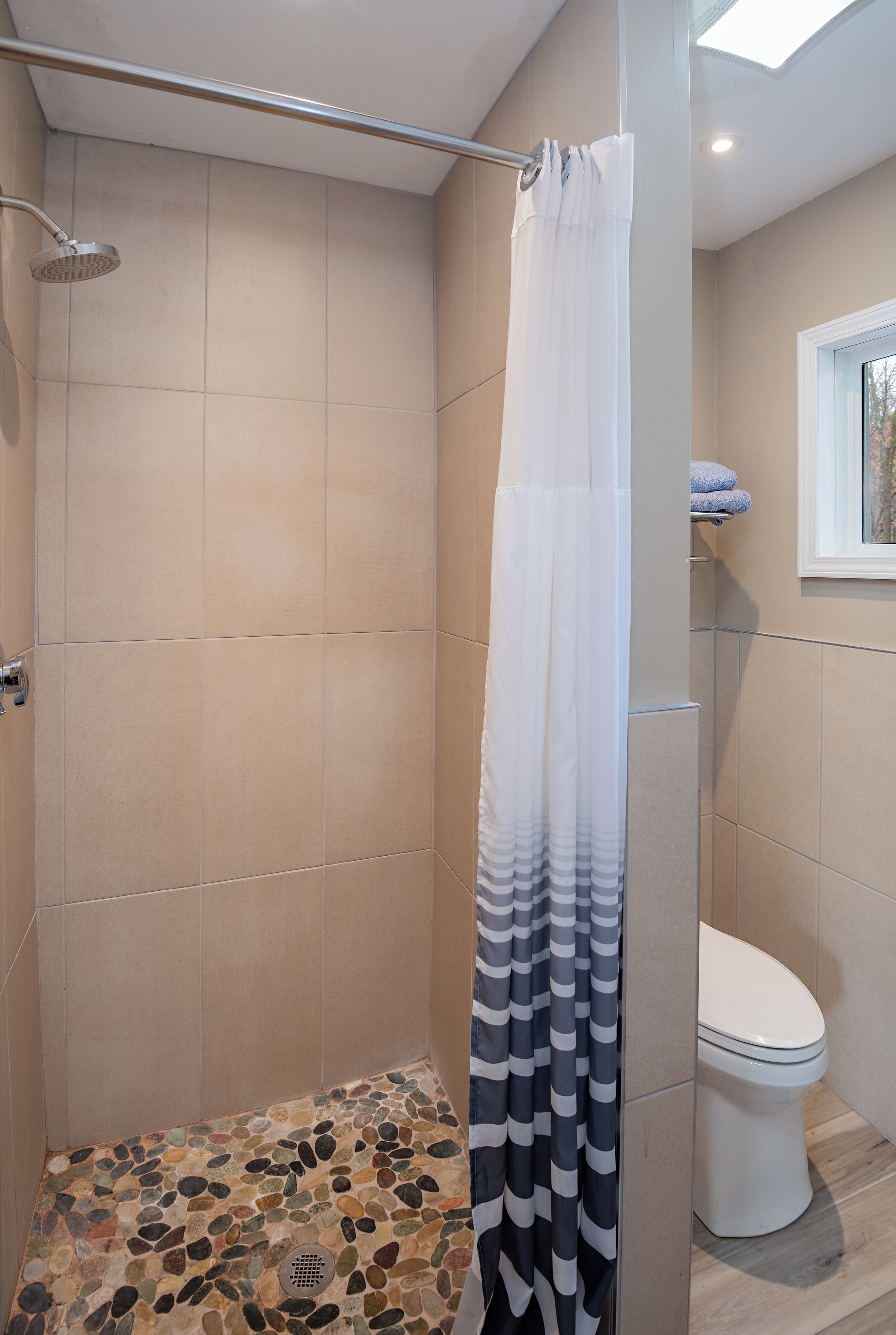 A shower with a rain showerhead, a black and white striped shower curtain, and a tiled floor with a pebble pattern.