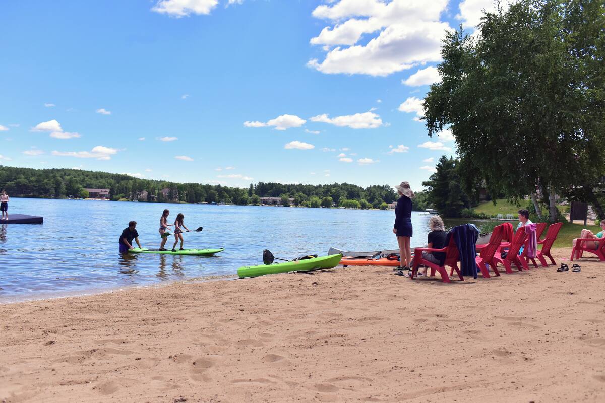 A lakeside beach with kayaks, a dock, and red chairs.
