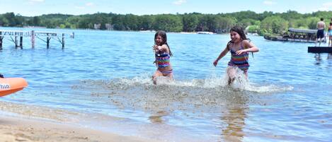 Two children playing in shallow water near a beach with a dock in the background.
