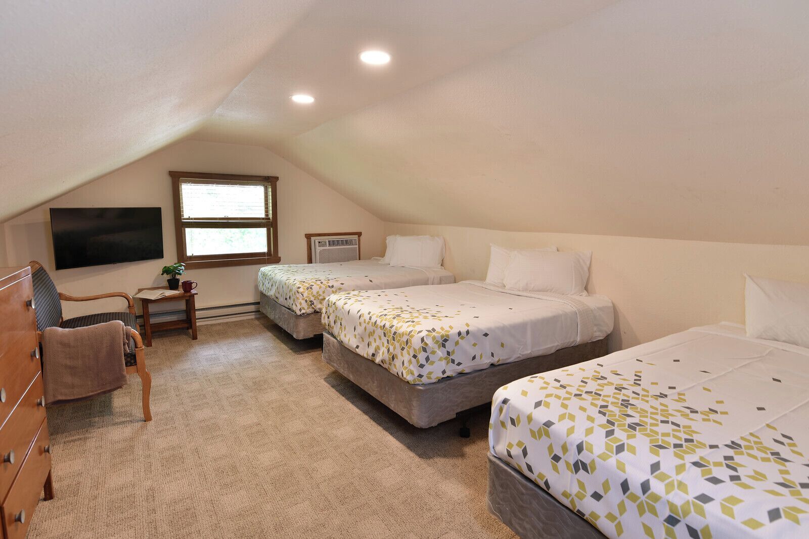 A bedroom with three beds, a TV, a desk, and a window.
