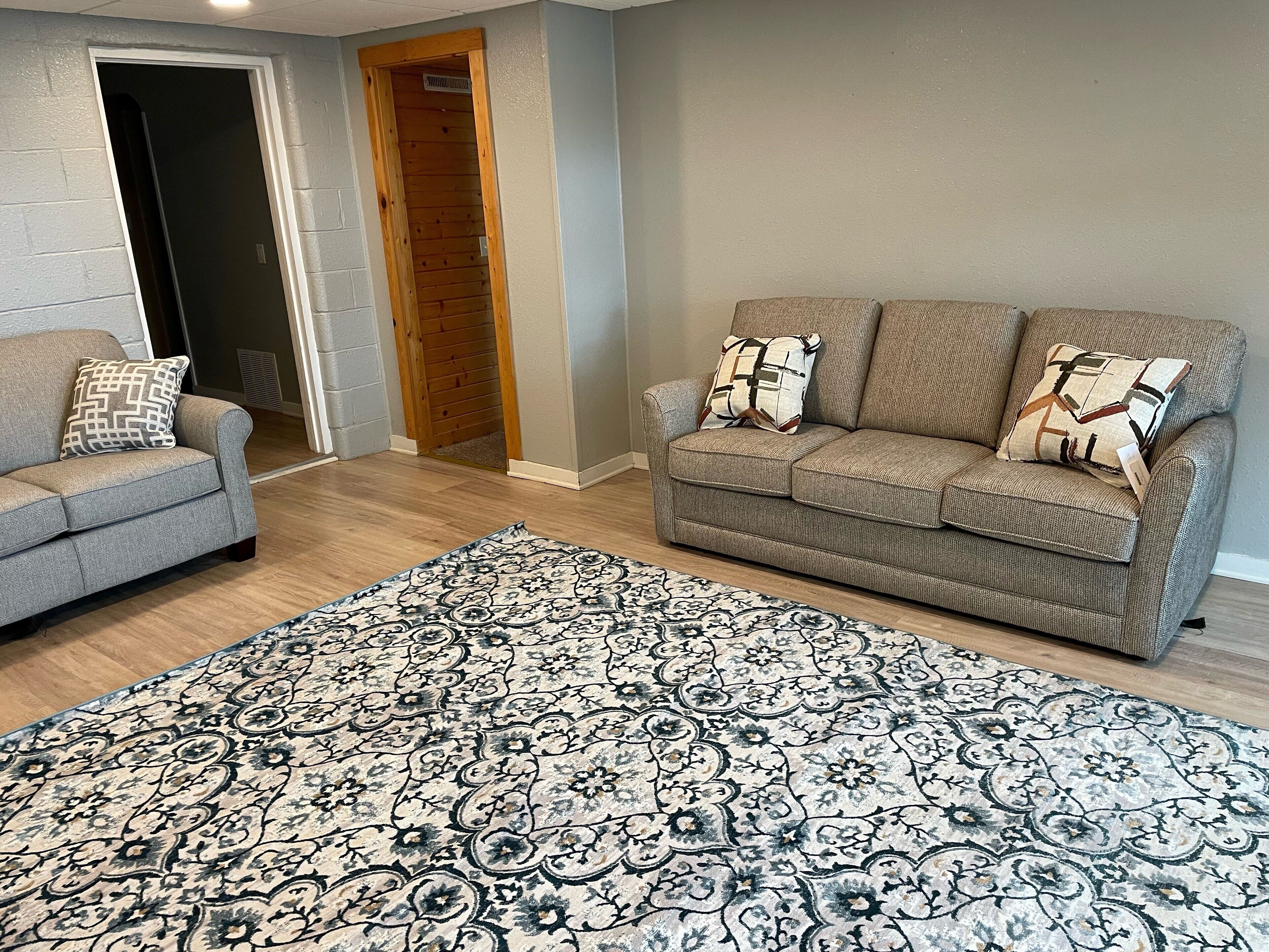 Un salon avec deux canapés gris, un tapis à motifs et une porte en bois.