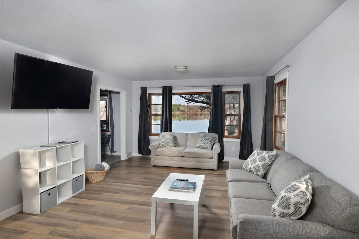 A living room with a sofa, a coffee table, a TV, and a view of a lake.