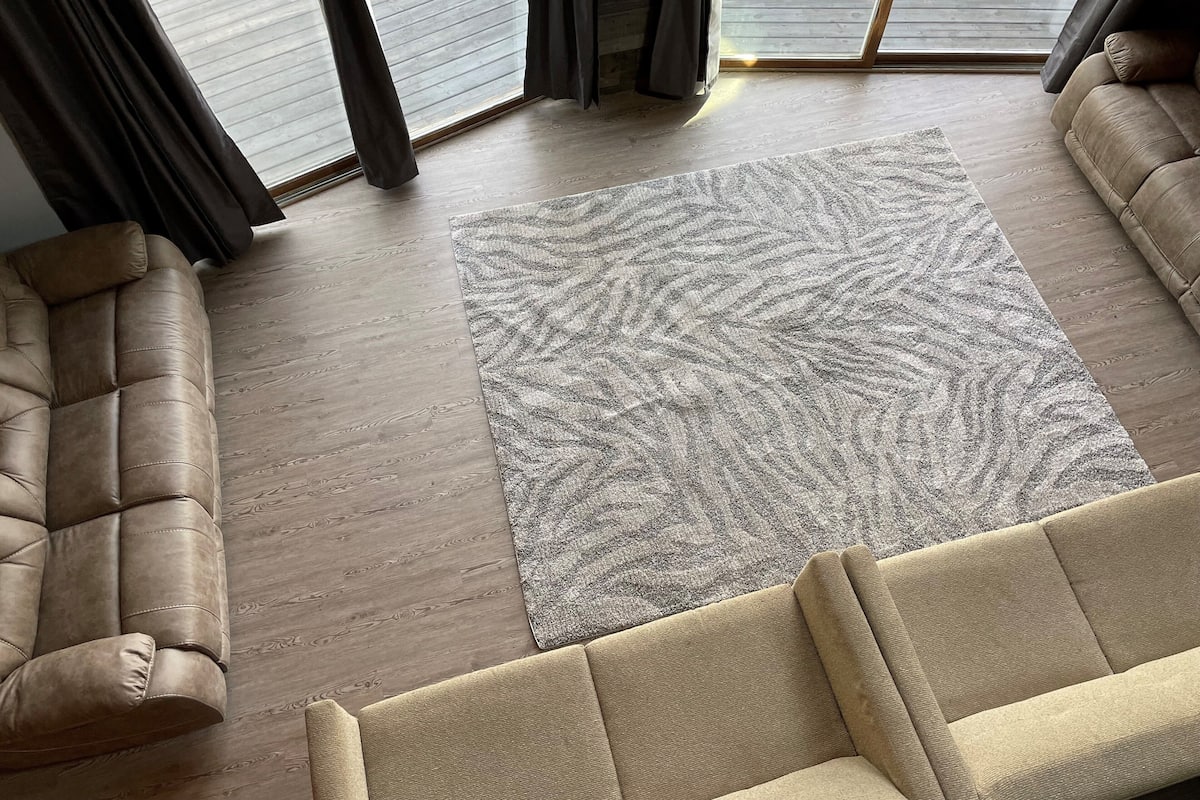 A living room with a beige sofa, a patterned rug, and a wooden floor.
