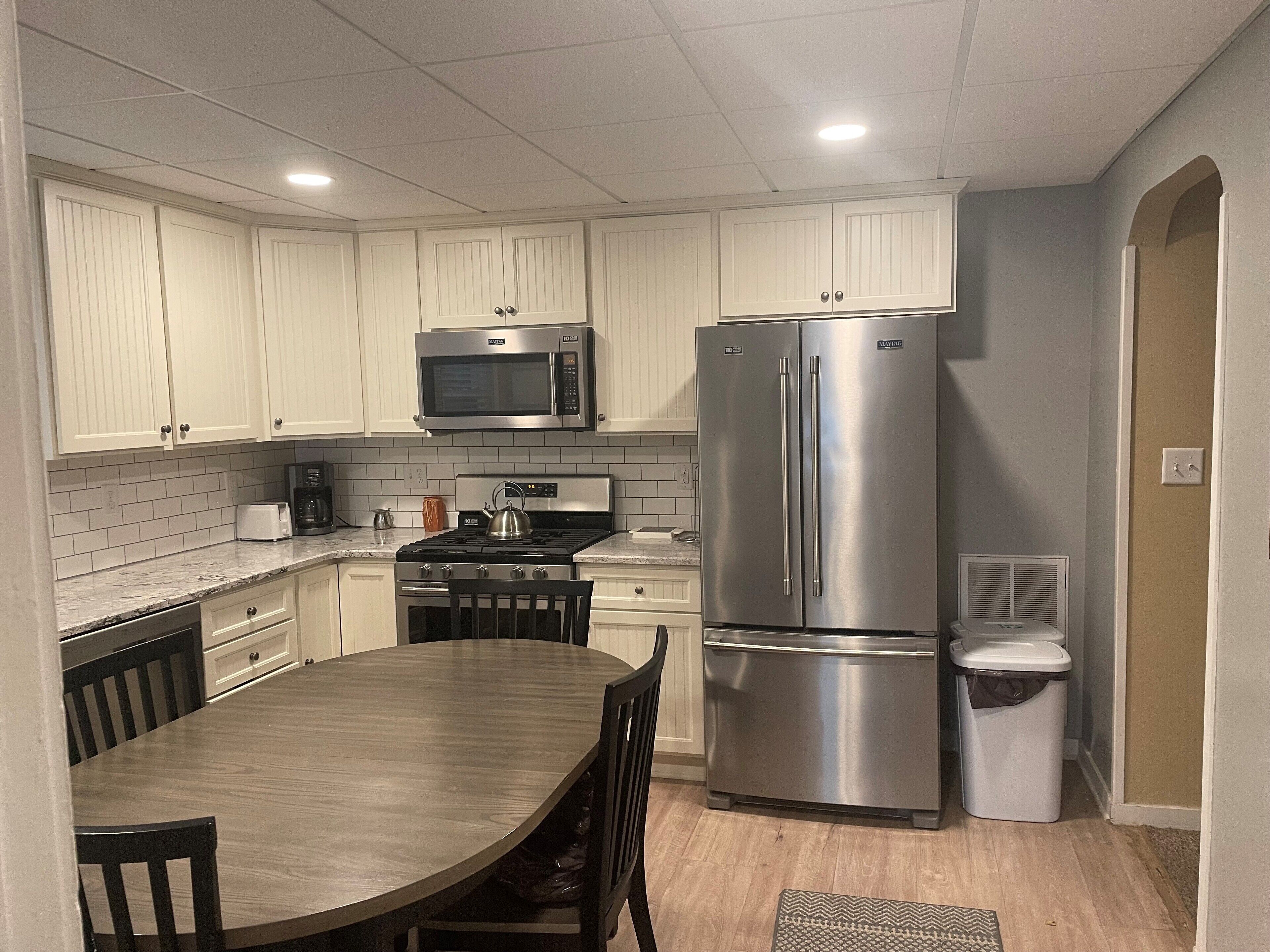 A compact kitchen with white cabinets, a stainless steel refrigerator, a microwave, and a gas stove.