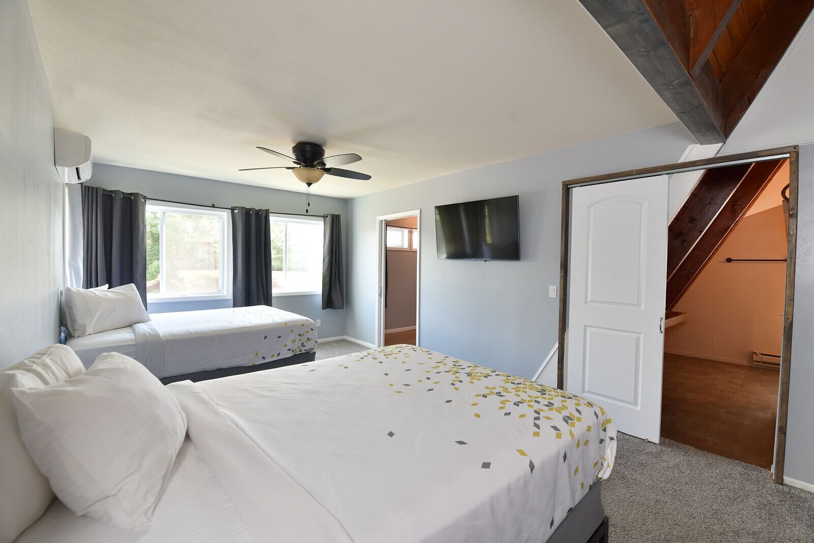 A bedroom with a bed, a ceiling fan, a TV, and a staircase leading to an upper level.