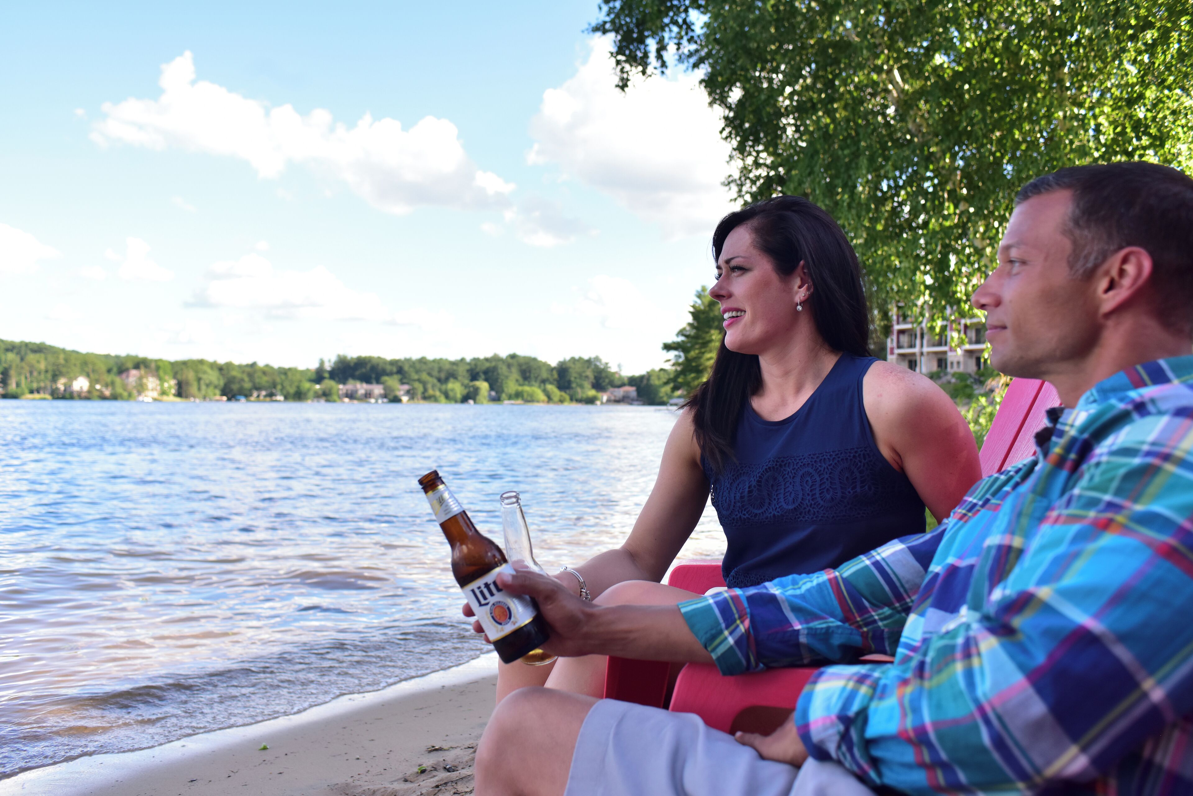 Two people sitting by a lake, one holding a beer bottle.