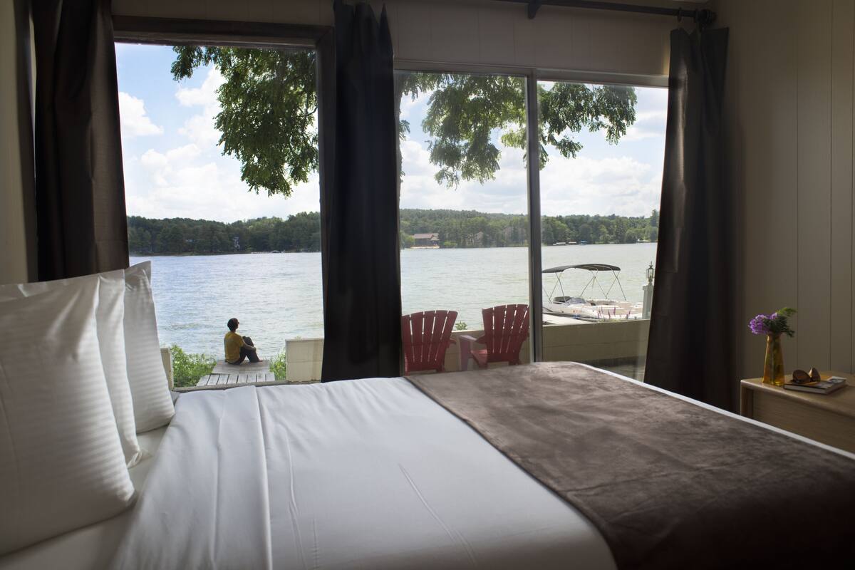 A bedroom with a large bed, a view of a lake, and a chair outside the window.