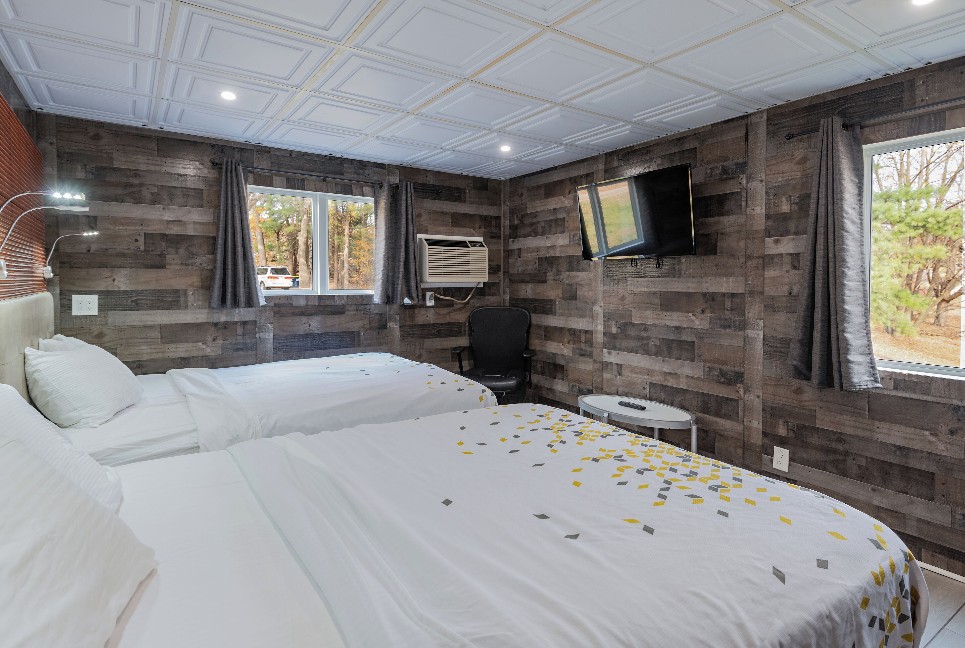 Une chambre d’hôtel avec deux lits, un téléviseur fixé au mur et une fenêtre avec des rideaux.